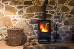 The interior of a cosy, stone cottage with stone walls and a fireplace with logs burning in a wood burner on a fireplace and hearth.